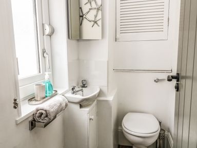 A small bathroom with a toilet and a sink with a mirror and a window with a towel cup and soap at Harbour Hideaway in Looe