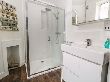 A bathroom with a glass shower enclosure white sink cabinet a mirror cabinet and a decorative sign on the wall at Harbour Hideaway in Looe