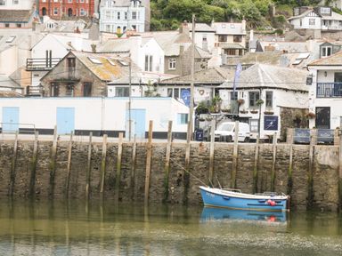 A small blue boat tied to wooden posts in a harbor with stone buildings and houses in the background at Harbour Hideaway in Looe