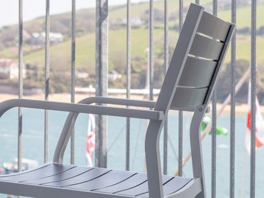 A gray metal chair on a balcony overlooking water and hills at 32 The Salcombe in Salcombe