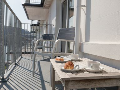 A balcony with two chairs a wooden table with croissants and cups at 32 The Salcombe in Salcombe