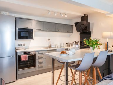 A modern kitchen with grey cabinets a refrigerator oven microwave and a countertop with chairs and tulips at 32 The Salcombe in Salcombe