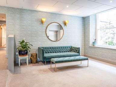 A sitting area with a teal sofa and bench a small table with a plant a round mirror and wall lights near a window at 32 The Salcombe in Salcombe