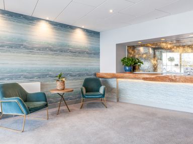 A waiting area with two blue chairs a small round table with a plant and a reception desk at 32 The Salcombe in Salcombe