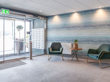 A lobby area with two armchairs a small round table with a plant a radiator a glass sliding door and a wall with a horizontal striped pattern at 32 The Salcombe in Salcombe