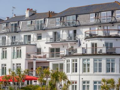 White multi-story building with balconies and outdoor furniture and palm trees in front at 32 The Salcombe in Salcombe