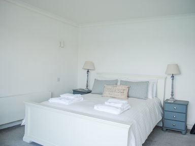 A bedroom with a white bed linens striped pillows two bedside tables with lamps and folded towels at 32 The Salcombe in Salcombe