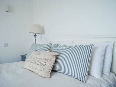 A bed with striped and printed cushions and a lamp on a bedside table at 32 The Salcombe in Salcombe
