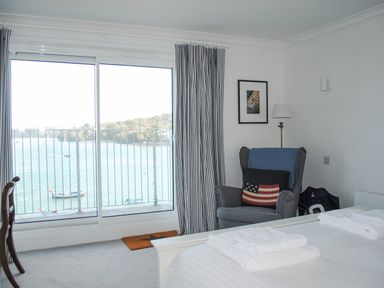 A bedroom with a bed a chair with a cushion a lamp and a sliding door with a view of water at 32 The Salcombe in Salcombe