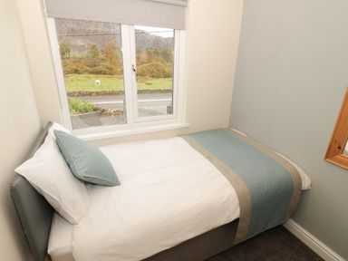 A small bedroom with a single bed by a window showing a view of trees and hills at Bryn in Bethesda