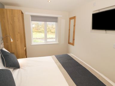 A bedroom with a bed pillows wooden wardrobe wall mirror and a mounted television at Bryn in Bethesda