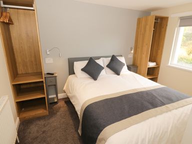 A bedroom with a double bed two wooden wardrobes bedside tables and a window at Bryn in Bethesda