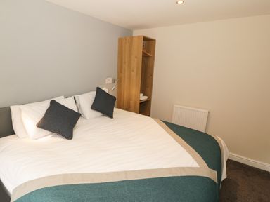 A bedroom with a bed with white sheets and dark pillows and a wooden open wardrobe at Bryn in Bethesda