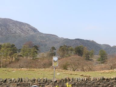 A rural landscape with grassy field trees and a rocky mountain in the background at Bryn in Bethesda