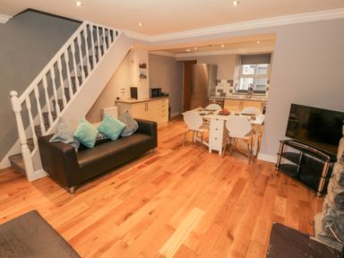 An open-plan living room and kitchen with a staircase a sofa with cushions a dining table with chairs a refrigerator and a television at Annest in Bethesda