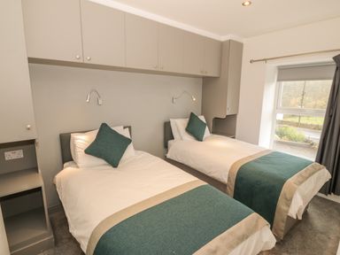 A bedroom with two single beds blue and beige bed runners overhead cabinets and a window with curtains at Annest in Bethesda