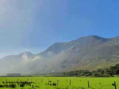A green field with sheep and fence posts in front of a mountain range under a clear blue sky at Annest in Bethesda