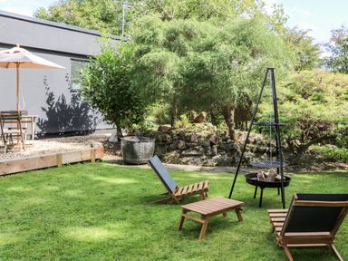 A garden with wooden chairs and table a fire pit and a patio area with an umbrella at Kub House in Wigginton Hertfordshire
