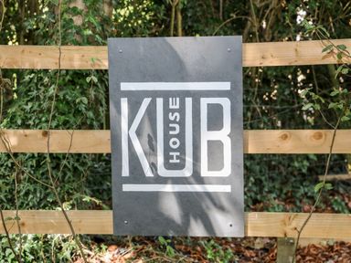 A gray sign with white text reading Kub House attached to a wooden fence with green foliage in the background at Kub House in Wigginton Hertfordshire