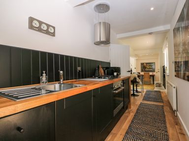 A kitchen with wooden countertop black cabinets a sink and stove with a rug on the wooden floor at Kub House in Wigginton Hertfordshire