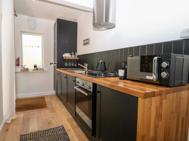 A narrow kitchen with black cabinets wooden countertops a gas stove oven microwave and a small window at Kub House in Wigginton Hertfordshire