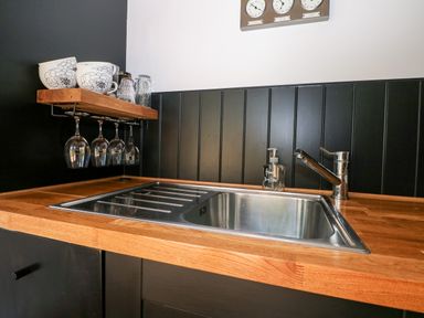 A kitchen sink with a wooden countertop and shelf holding cups and glasses at Kub House in Wigginton Hertfordshire
