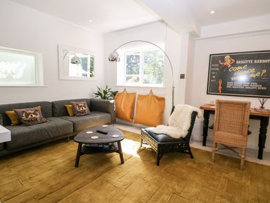 A living room with a grey sofa, coffee table, two orange bean bags, an accent chair, desk with a wicker chair, and a framed poster at Kub House in Wigginton Hertfordshire
