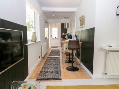 A narrow dining area with a wooden table and bar stools alongside a kitchen with black cabinets and a window at Kub House in Wigginton Hertfordshire