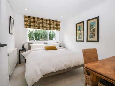 A bedroom with a bed white bedding a wooden desk and chair two framed pictures on the wall and a window with patterned blinds at Kub House in Wigginton Hertfordshire