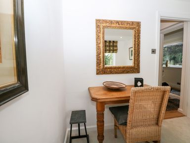 A small wooden desk with a woven chair and a decorative bowl under a framed mirror at Kub House in Wigginton Hertfordshire