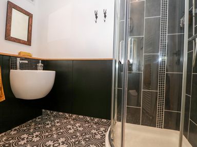 A bathroom with a wall-mounted sink mirror towel and glass shower enclosure with tiled walls at Kub House in Wigginton Hertfordshire