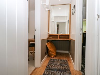 A hallway with wooden flooring a patterned runner rug a large mirror on the wall a small wooden desk with an orange cushion underneath at Kub House in Wigginton Hertfordshire