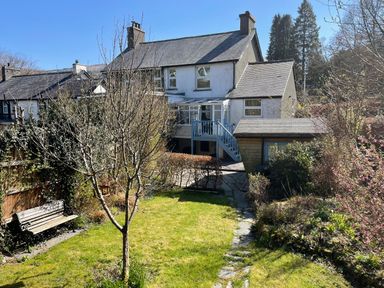A garden with grass trees bushes a bench and a stone path leading to a house at 7 Castle Terrace in Dolwyddelan