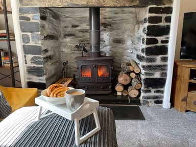 A living room with a wood burning stove firewood and a tray with a cup and pastries at 7 Castle Terrace Dolwyddelan