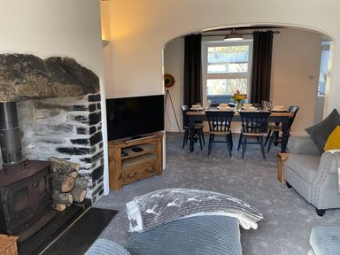 A living room with a wood burning stove television and a dining table set for six at 7 Castle Terrace in Dolwyddelan