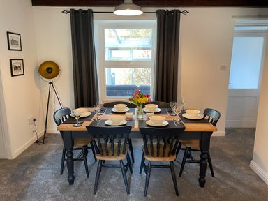 A dining room with a rectangular table set for six with black chairs and flower vase at 7 Castle Terrace in Dolwyddelan
