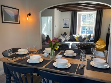 A dining table set with bowls and glasses next to a living room with a sofa and pillows at 7 Castle Terrace in Dolwyddelan