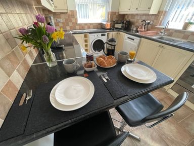 A kitchen counter set for two with plates, cups, croissants, cookies, a french press, and a vase of flowers at 7 Castle Terrace in Dolwyddelan