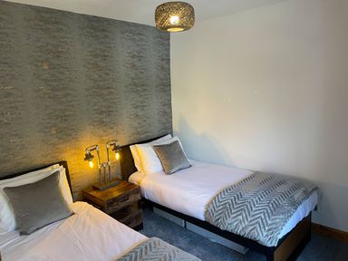 A bedroom with two single beds separated by a wooden nightstand with lamps at 7 Castle Terrace in Dolwyddelan