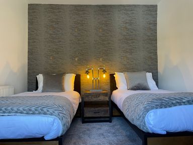 A bedroom with two single beds and a nightstand with a lamp between the beds at 7 Castle Terrace in Dolwyddelan