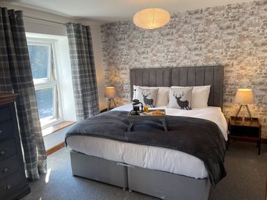 A bedroom with a double bed with pillows and a breakfast tray beside a window with plaid curtains at 7 Castle Terrace in Dolwyddelan
