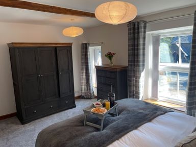 A bedroom with dark wooden wardrobe and chest of drawers with flowers and breakfast tray on bed at 7 Castle Terrace in Dolwyddelan