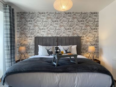 A bedroom with a bed with grey headboard two lamps on bedside tables and a tray with breakfast at 7 Castle Terrace in Dolwyddelan