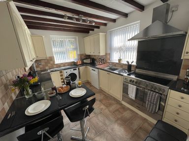 A kitchen with a stove sink dishwasher and breakfast bar with two stools at 7 Castle Terrace in Dolwyddelan
