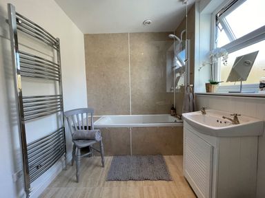 A bathroom with a bathtub shower combination a sink towel rail and a chair with towel at 7 Castle Terrace in Dolwyddelan