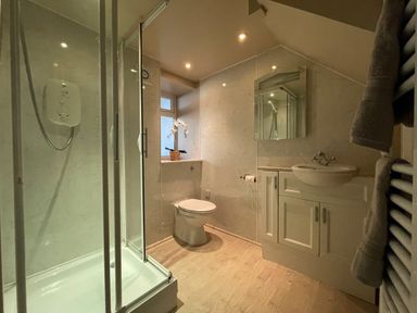 A bathroom with a shower, toilet, sink with cabinet, mirror, and towel rack at 7 Castle Terrace in Dolwyddelan