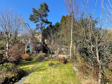 A garden with grass a stone path small trees shrubs and garden sheds at 7 Castle Terrace in Dolwyddelan