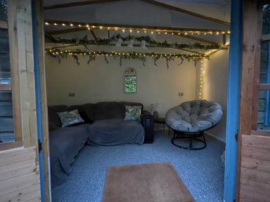 A small room with a sofa and a round cushioned chair with decorative lights and greenery on the ceiling at 7 Castle Terrace in Dolwyddelan