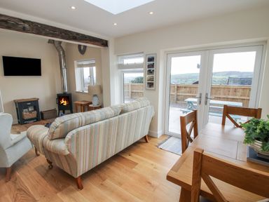 A living room with a striped sofa a wood stove a television wooden dining table and chairs with glass doors showing an outdoor picnic bench at Border View Lodge in Llandrinio