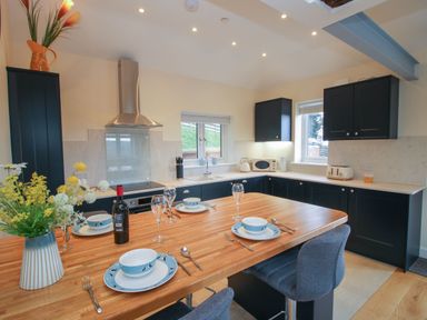 A kitchen with black cabinets and a wooden dining table set with tableware and wine at Border View Lodge in Llandrinio